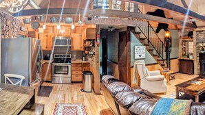 Un intérieur chaleureux et rustique comprenant une cuisine, un coin salon et un escalier.