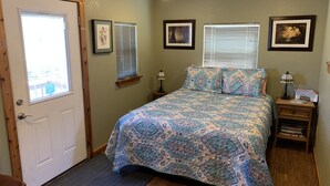 A bedroom with a bed, two bedside tables, a door, and two windows with blinds. - Welcome to Bandera Stronghold - Red Cloud Cabin (Bandera)