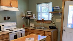 A kitchen with wooden cabinets, a stove, a sink, and a ceiling fan. - Welcome to Bandera Stronghold - Red Cloud Cabin (Bandera)