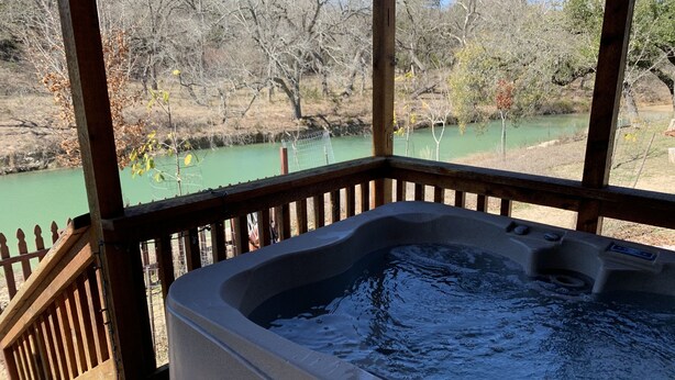 A hot tub on a wooden deck with a view of a river and trees. - Welcome to Bandera Stronghold - Red Cloud Cabin (Bandera)