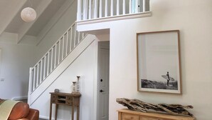 Une pièce spacieuse avec un plafond haut, un escalier en bois, un ventilateur de plafond et un coin repas comprenant une table et des chaises.