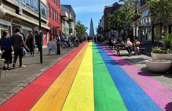 Une rue avec un chemin piétonnier aux couleurs de l’arc-en-ciel, des bâtiments et une tour imposante en arrière-plan.