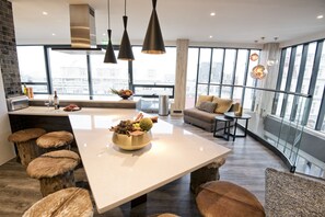 A modern kitchen with a large island, stools, and a view of the city through large windows.