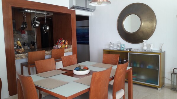 A dining area with a wooden table and chairs, a kitchen area with hanging pots, and a decorative mirror on the wall. - Amazing Beach Front Apartment, 3 BDRMS, 3 Baths, Sleeps 8, (Cancun)