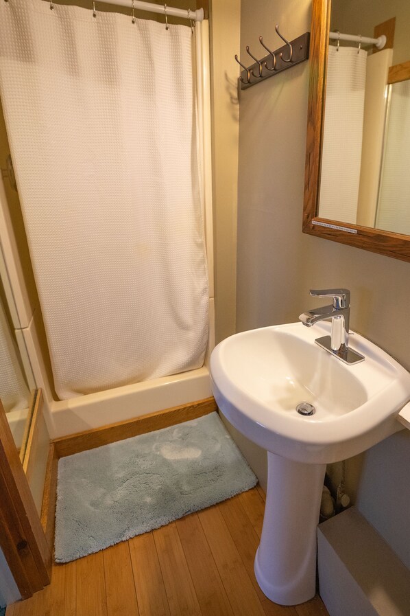 A bathroom with a bathtub, a white sink, a wooden floor, and a blue rug.