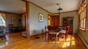 A spacious room with wooden flooring, a dining area with chairs and a table, and a kitchen area with cabinets and a window. - Hyde Park Village Home near STOWE -- 4BR bedroom (Hyde Park)