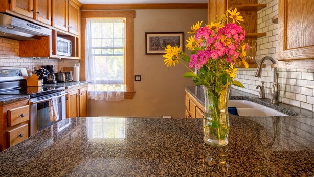 A kitchen with wooden cabinets, a granite countertop, a sink, and a vase with flowers. - Hyde Park Village Home near STOWE -- 4BR bedroom (Hyde Park)