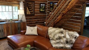 Un interior de cabaña acogedor, con un sofá de cuero, una manta de piel y un interior de madera rústica.