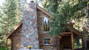 Una cabaña de troncos con chimenea de piedra, fachada de madera y un porche con leña apilada.