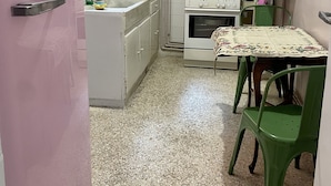 Una cocina pequeña con un refrigerador rosa, armarios blancos, una estufa y una mesa con sillas.
