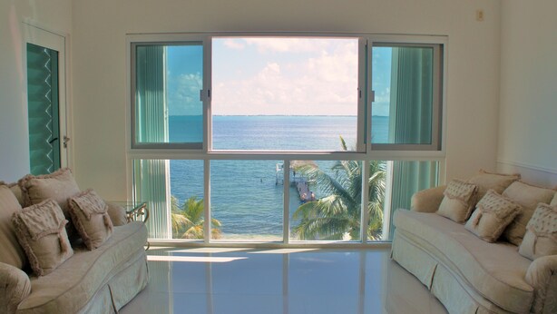 Een ruime woonkamer met een groot raam met uitzicht op de oceaan en palmbomen.