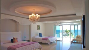 Een hotelkamer met twee bedden, een kroonluchter, een groot raam met uitzicht op de oceaan en een zithoek met uitzicht.