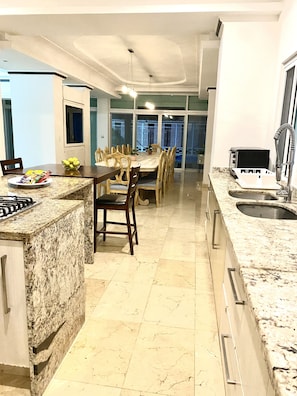 A modern kitchen with granite countertops, a dining area with wooden chairs, and a large window. - PRIVATE BEACH HOUSE FOR BIG FAMILIES 7BR (Sleeps 20) Cancun, Punta Sam  (Cancún)