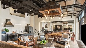 A spacious living area with a high ceiling, exposed beams, and a modern kitchen in the background. - Inn Cahoots on 6th: 15 BR/39 Beds, Pool, Roofdeck (Austin)
