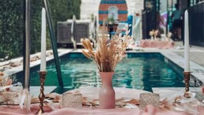A poolside setting with a table adorned with candles, dried flowers, and a vase. - Inn Cahoots on 6th: 15 BR/39 Beds, Pool, Roofdeck (Austin)