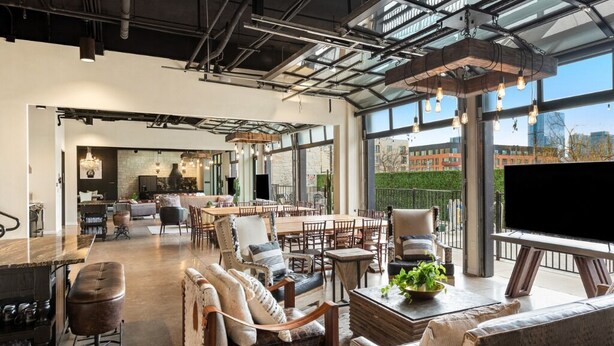A spacious, modern living area with a large dining table, comfortable seating, and a large window offering a city view. - Inn Cahoots on 6th: 15 BR/39 Beds, Pool, Roofdeck (Austin)