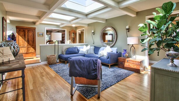 A spacious living room with a high ceiling, skylights, a blue sofa set, a wooden coffee table, and a large plant. - CARMEL OASIS-Gorgeous Views 4 Bedroom 2.5- EXCEPTIONAL RATINGS (Carmel-By-The-Sea)