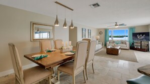 A dining area with a wooden table, chairs, and hanging pendant lights. There is a living room with a sofa, a coffee table, and a television.