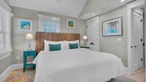 A bedroom with a large bed, two nightstands, a ceiling fan, and artwork on the walls.