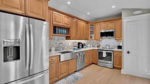 A modern kitchen with stainless steel appliances, wooden cabinets, and a tiled backsplash.