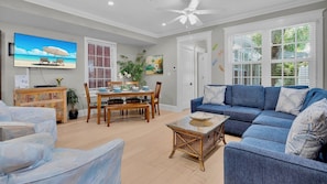 A living room with a blue sofa, wooden dining table, and a television displaying a beach scene.