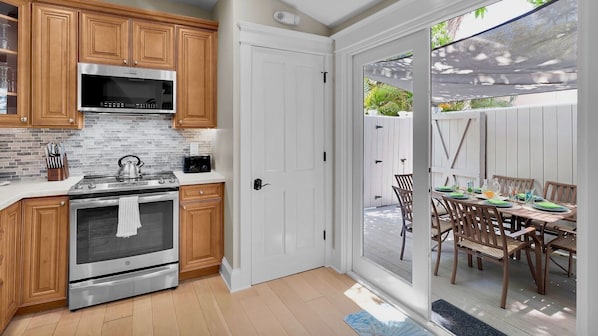 Una cucina con mobili in legno, forno in acciaio inossidabile e forno a microonde. C'è una porta scorrevole in vetro che dà su un patio esterno con tavolo e sedie.