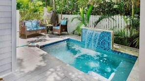 A swimming pool with a waterfall feature, surrounded by a deck and wicker furniture.