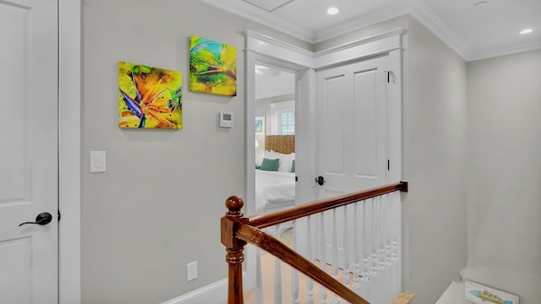 A hallway with a staircase, a door leading to a bedroom, and two abstract paintings on the wall.