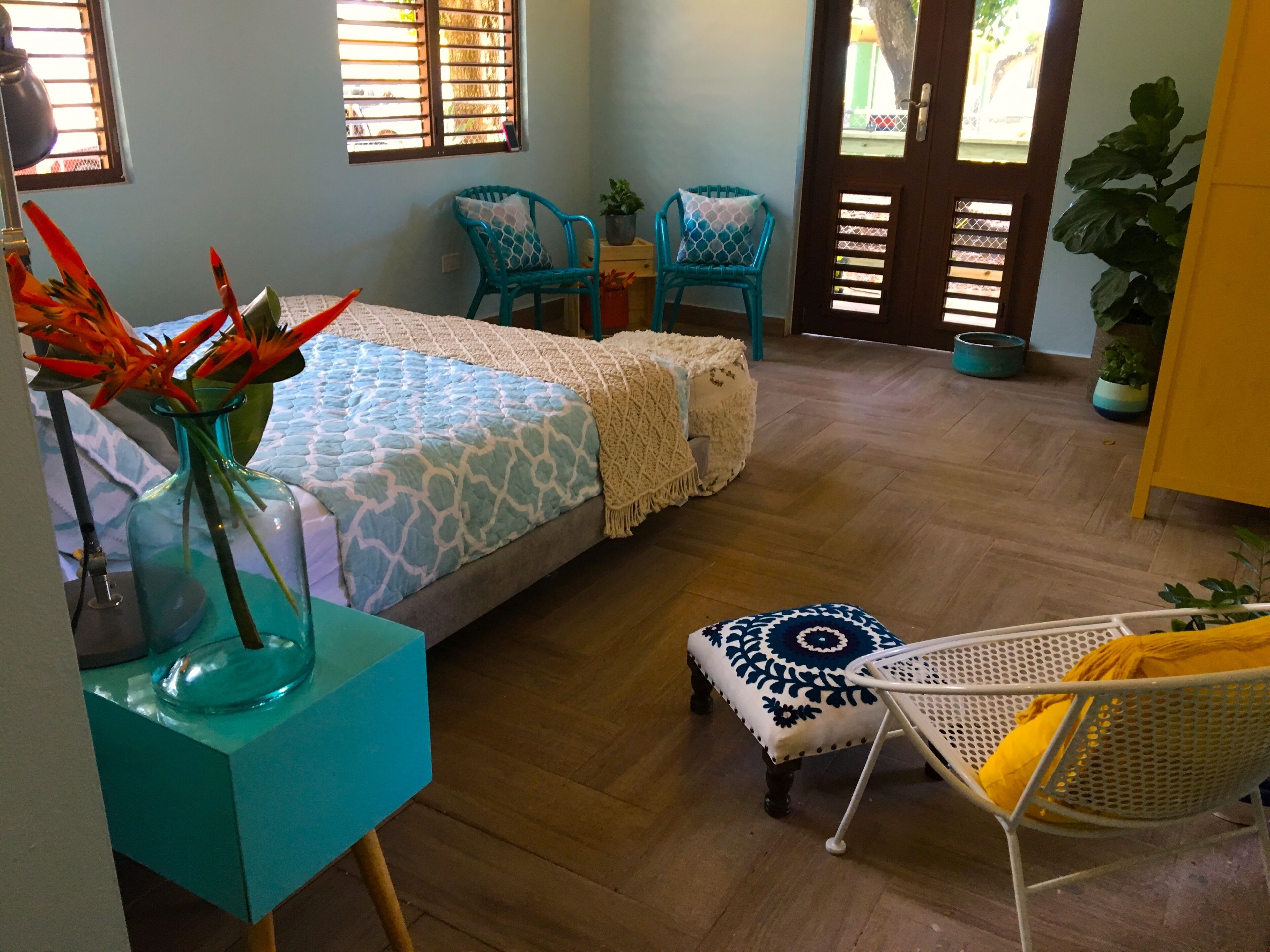 A bedroom with a bed, two chairs, a small table with a vase, and a door with a window.