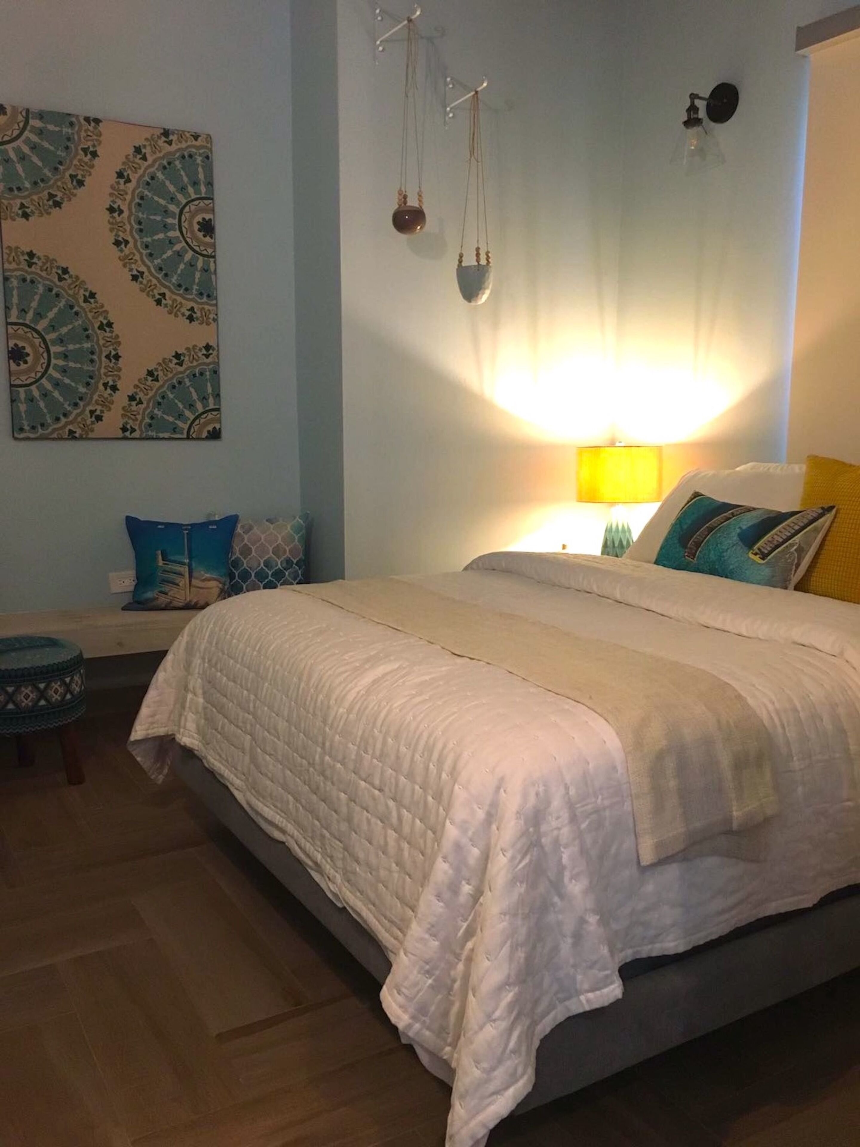 A bedroom with a bed, a bedside table, a wall-mounted lamp, and a decorative wall piece.