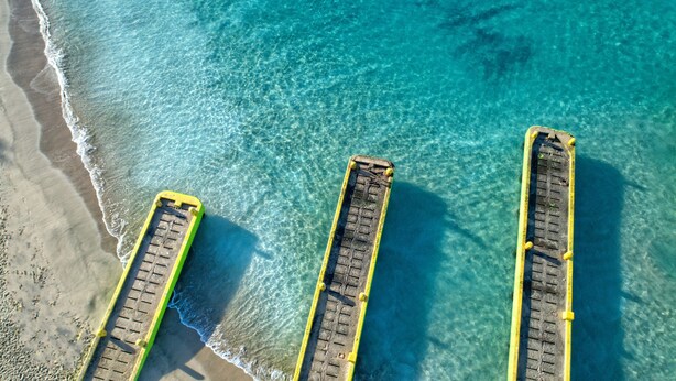 An aerial view of a beach with three yellow and green piers extending into the water.