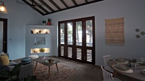 A dining area with a wooden table set for four, a sofa with cushions, and a wall-mounted shelf with plants.