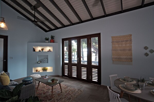 A dining area with a wooden table set for four, a sofa with cushions, and a wall-mounted shelf with plants.