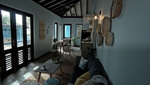 A spacious living area with a sofa, coffee table, and a dining table with chairs. There is a kitchen area in the background with a stove and cabinets.