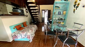 Un espacio habitable compacto con cama, una pequeña mesa de comedor con sillas, una zona de cocina con tostadora y una escalera.