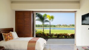 A bedroom with a large bed, a wooden door, and a view of a golf course and water. - Flat 701 Luxury Condo, Premier Golf Membership, Private Pool & Golf Cart (Punta Mita)