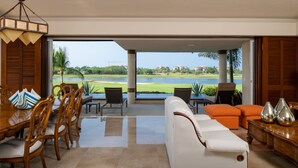 A spacious living area with a view of a lake and golf course, featuring a dining set, seating area, and a large window. - Flat 701 Luxury Condo, Premier Golf Membership, Private Pool & Golf Cart (Punta Mita)