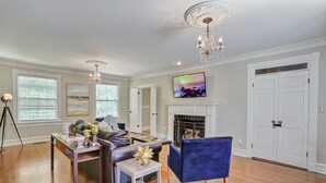 A living room with a fireplace, a television mounted above it, and a chandelier. - Huge Historic 4BR House w/  Patio, sleeps 12 (Jackson)