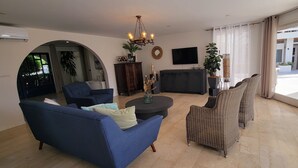 Ein Wohnzimmer mit blauem Sofa, Korbstühlen, einer dunklen Unterhaltungsecke und einem großen Fenster mit Vorhängen.