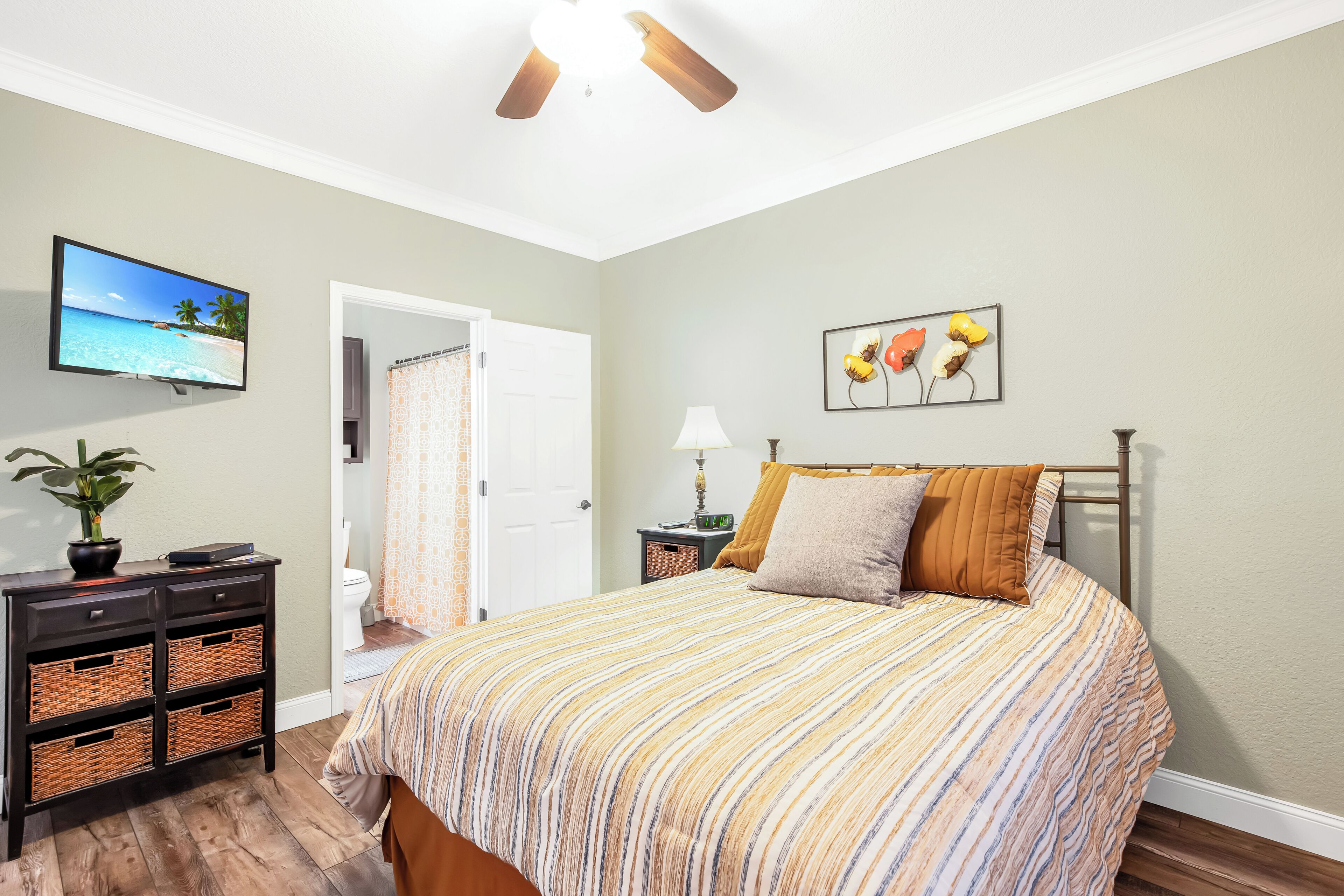 A bedroom with a bed, a television, a nightstand, a lamp, and a painting.