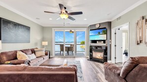 A spacious living room with a large window, a fireplace, and a ceiling fan. - View for Miles! Remodeled Lands' End Luxury Condo - Wifi, Waterpark, Pool, Docks (Osage Beach)