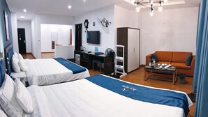 Ett hotellrum med två sängar, ett skrivbord, en tv, en soffa och ett matbord med tekannor.