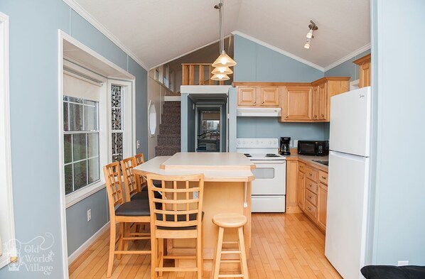 Una cocina compacta con armarios de madera, un refrigerador blanco, un microondas y un comedor con mesa y sillas.