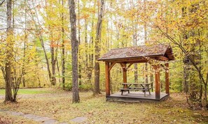 Un pabellón de madera con una mesa de picnic en un área boscosa.