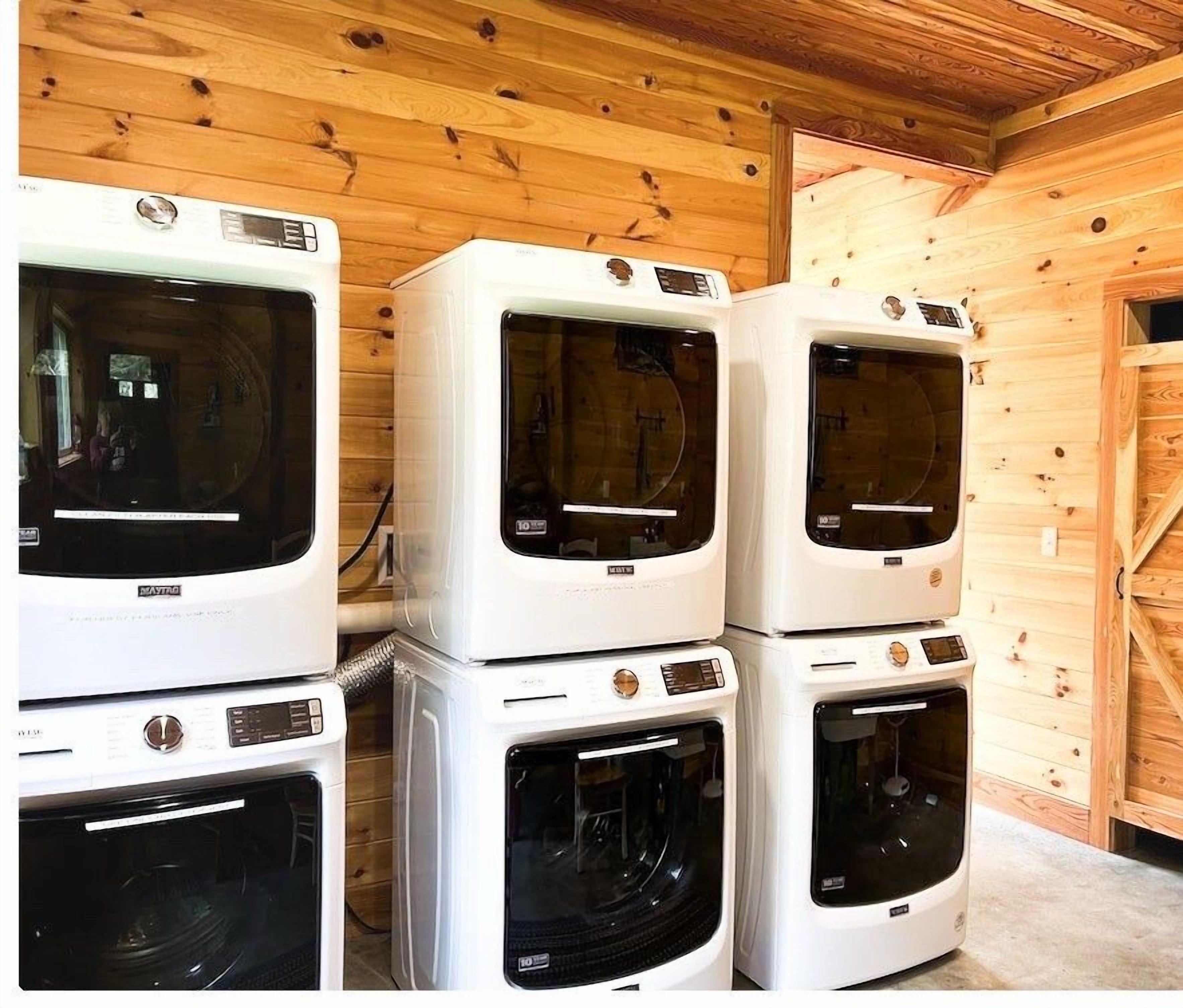A stack of white appliances, including a dryer and a washing machine, in a wooden room with a wooden door.