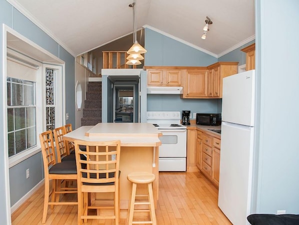 A compact kitchen with wooden cabinets, a white refrigerator, a microwave, and a dining area with a table and chairs.
