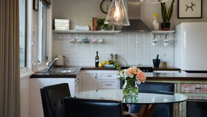 Et moderne køkken med et rundt glasbord, sorte stole, en hængende lampe og en vase med blomster.
