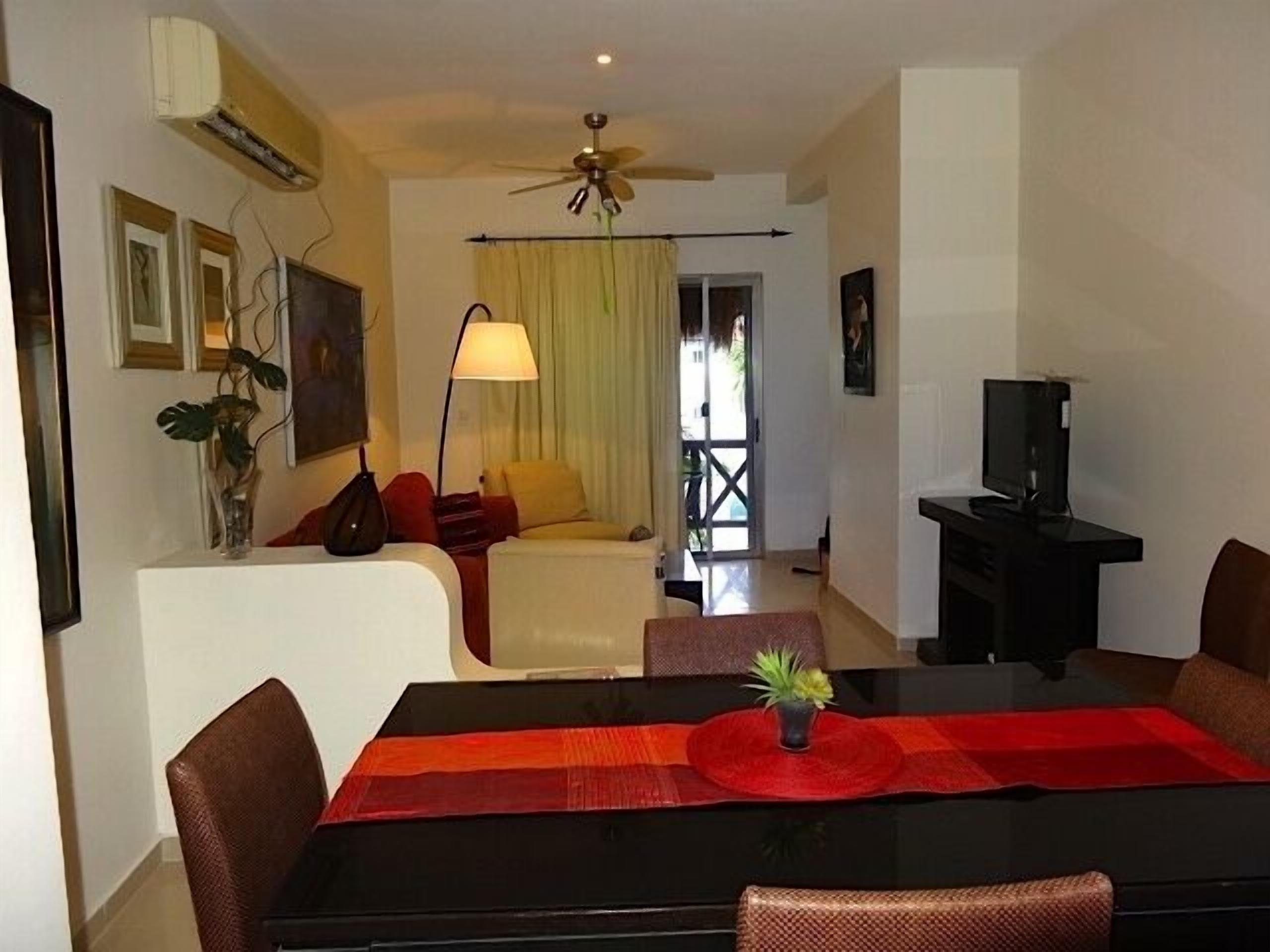 A hotel room with a dining table, chairs, a TV, a ceiling fan, and a window with curtains.