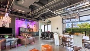 A spacious living area with a large TV, leather sofas, and a dining table with chairs. - Inn Cahoots on 6th: 5BR/13Beds - Pool, Rooftop, Garden Bars, Walk to Everything (Austin)
