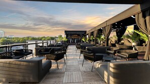 A deck with outdoor seating and a view of the city skyline at sunset. - Inn Cahoots on 6th: 5BR/13Beds - Pool, Rooftop, Garden Bars, Walk to Everything (Austin)